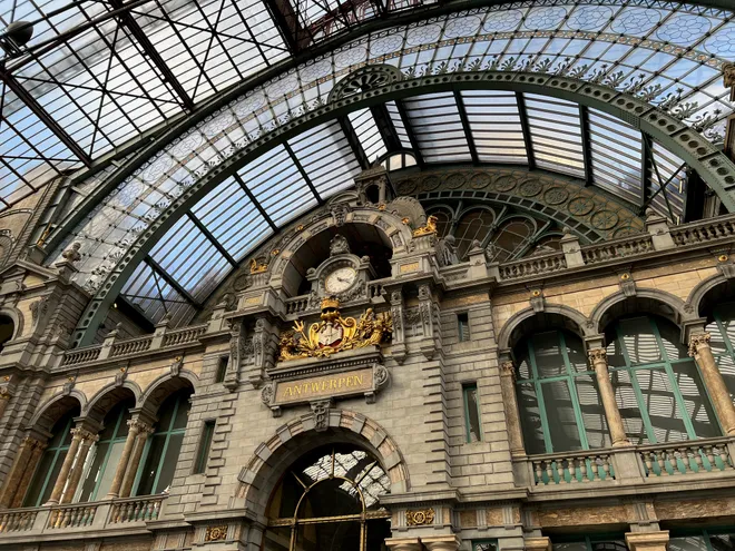 The vaulted iron and glass roof of Antwerp Central station above an ornate stone facade with a gilded clock