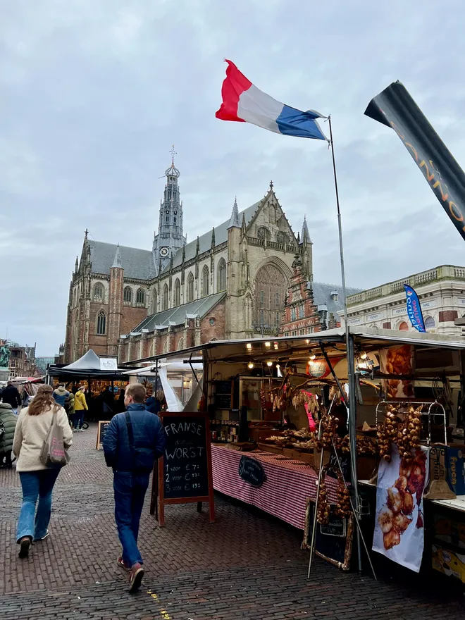 Market stalls in a cobbled square beneath a Dutch flag, a large Gothic church behind