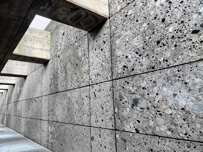 A wall of aggregate concrete panels receding down a covered walkway